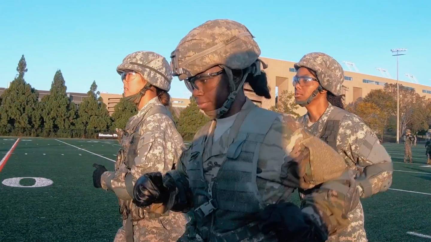 3 students run in a field in military fatigues