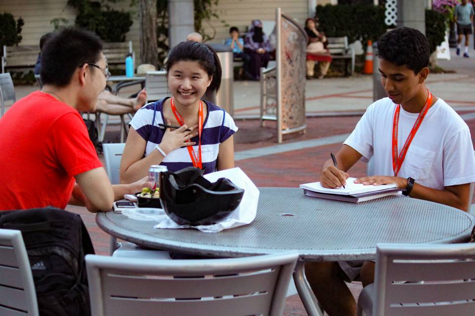 Students interviewing person sitting at outside cafe