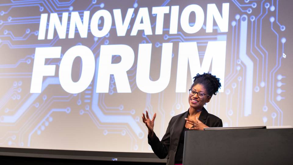 Zakiya Smith Ellis speaking in front of a screen with the words "Innovation Forum" on it