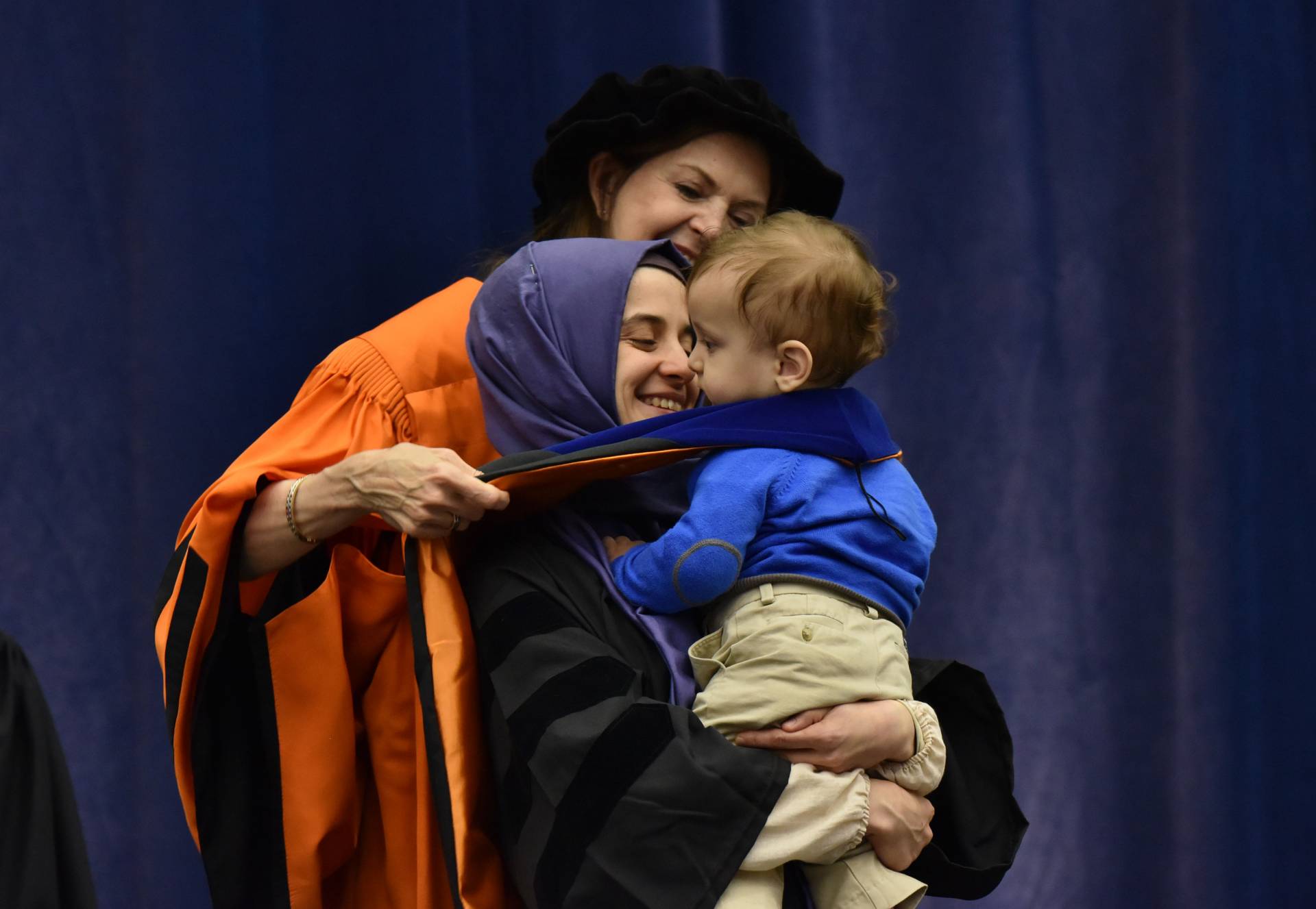 Student is hooded with child in arms
