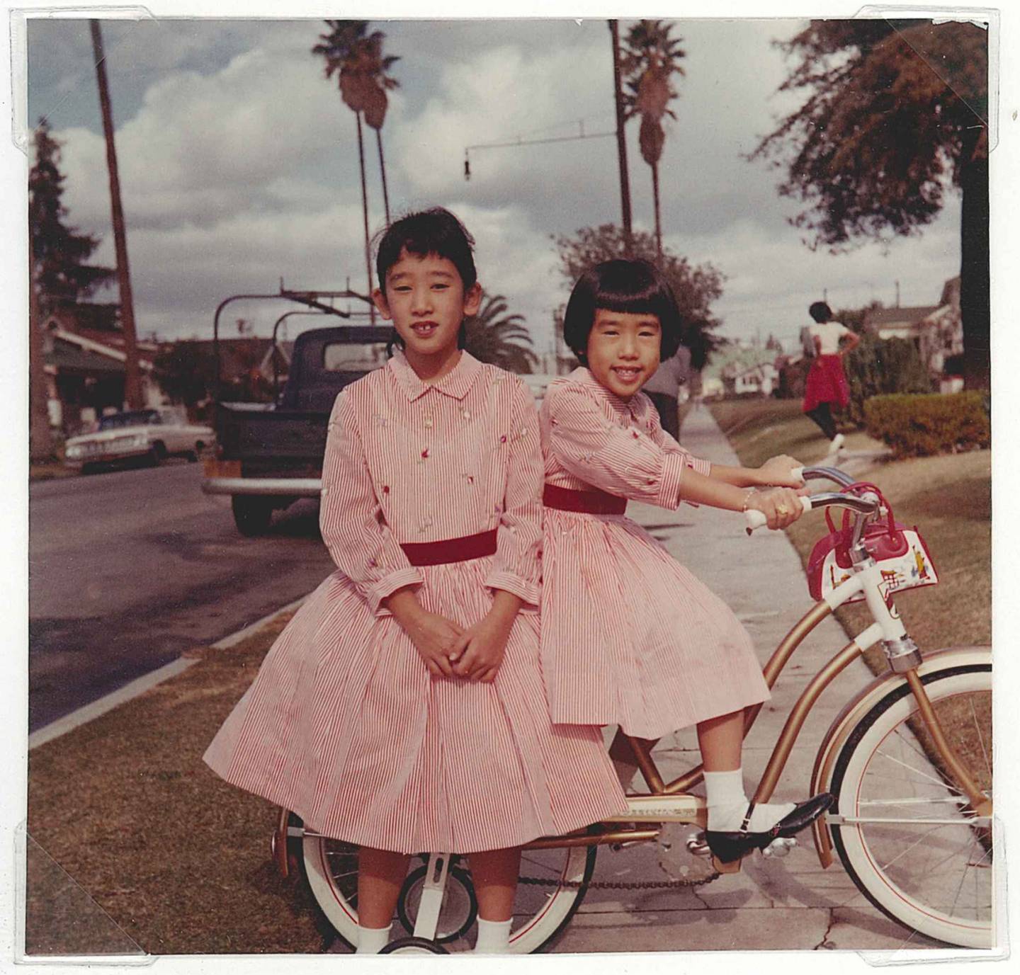Two girls in pink dresses with bicycles on Los Angeles sidewalk