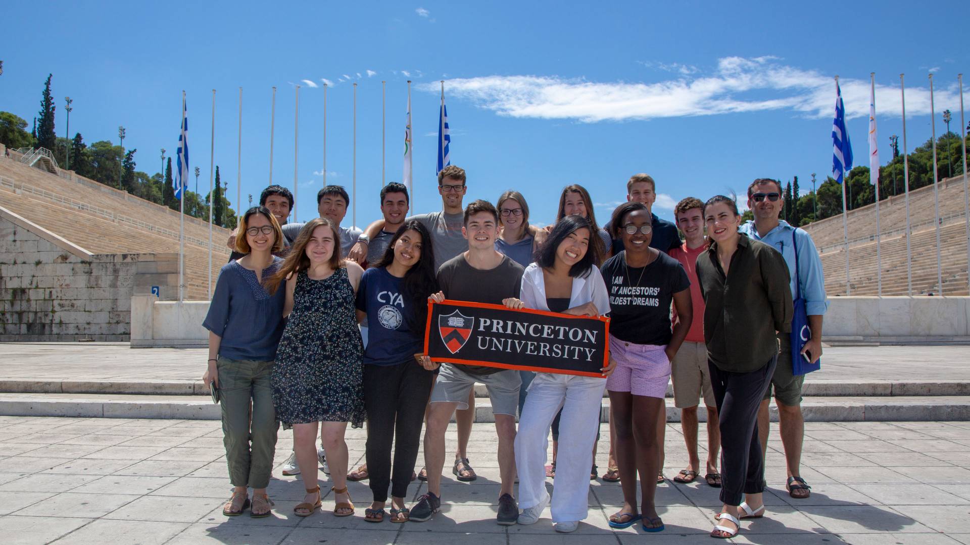Students and professor standing in front of stadium holding Princeton University banner
