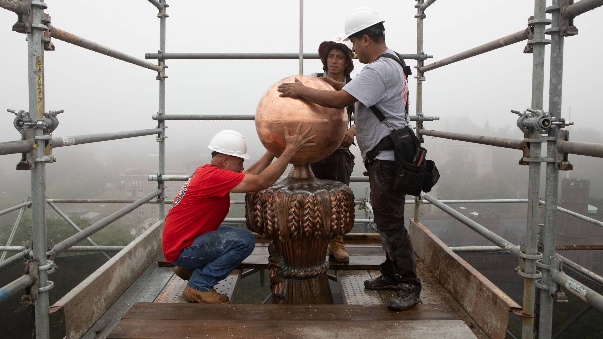 Workers assembling copper wheat-sheaf column and ball on top of Nassau Hall cupola