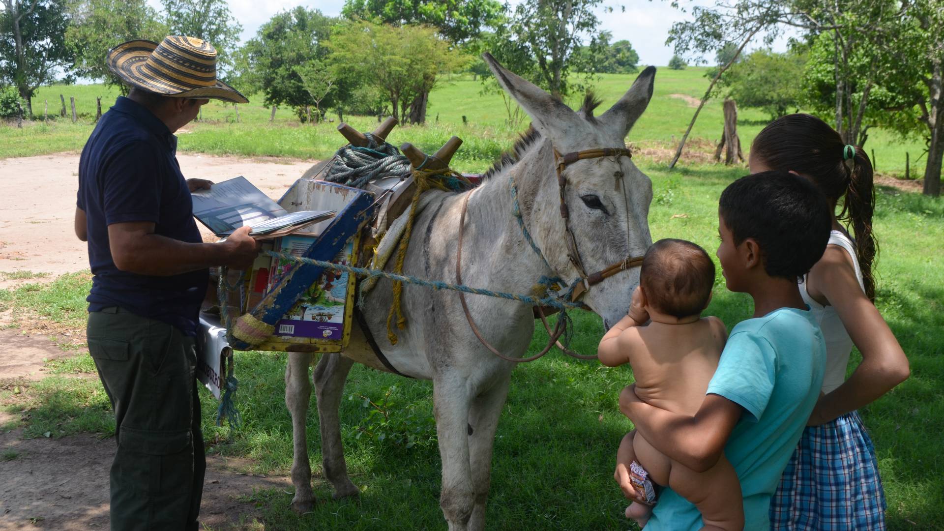 Man reading book in front of burro and three children