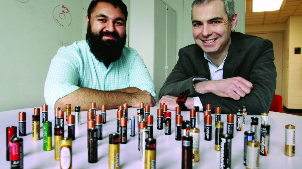 Photo showing two Princeton University researchers sitting at a table on which are displayed AA batteries that they use in their research.