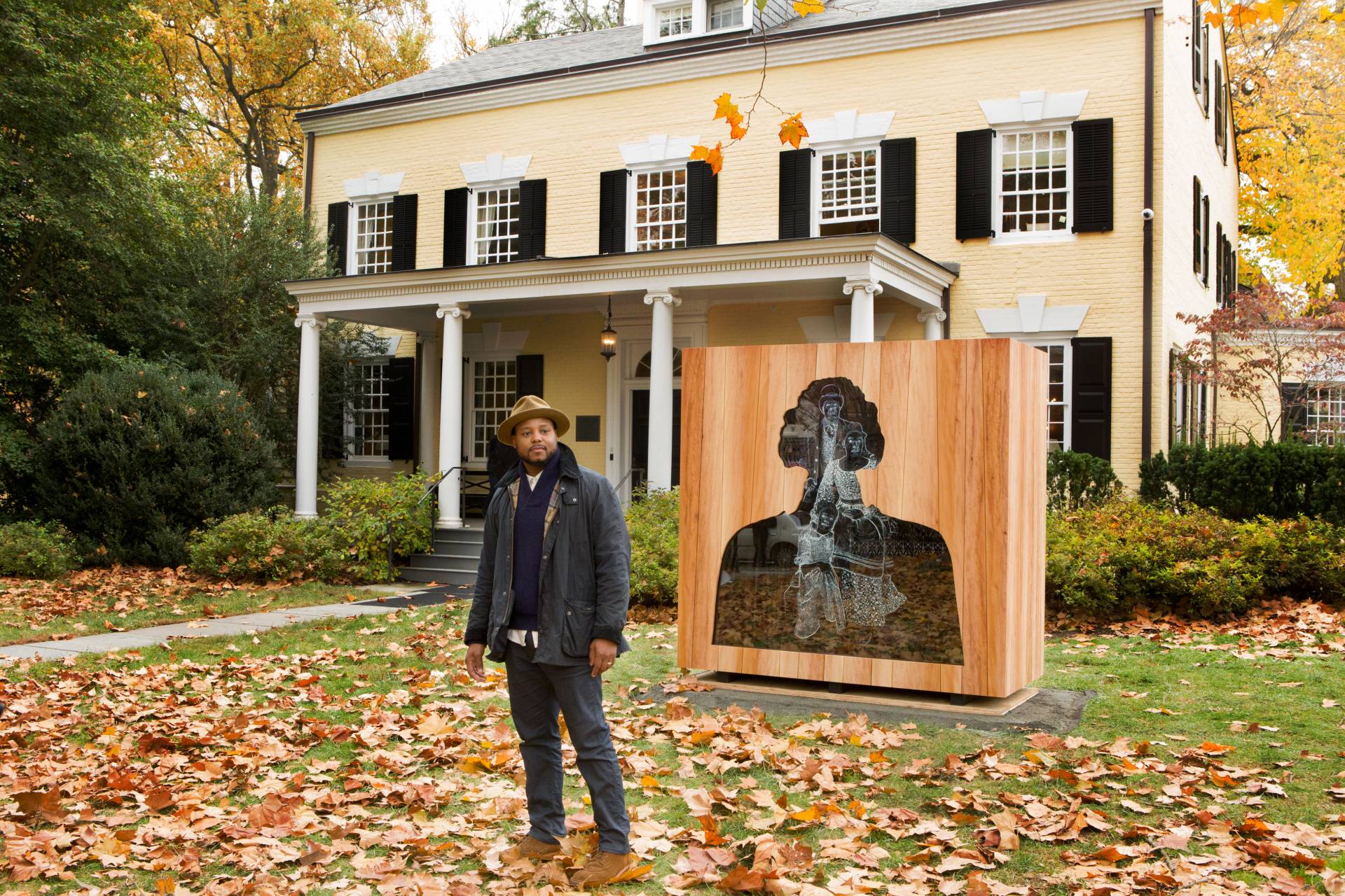 Titus Kaphar standing outside Maclean House in front of his sculpture