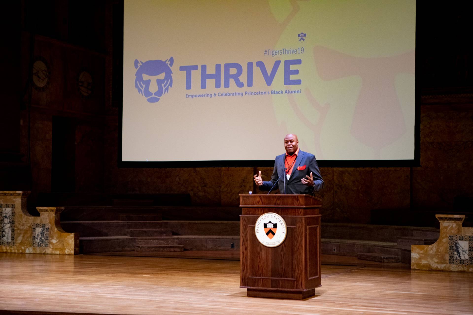 Craig Robinson speaking at podium in front of screen with the word THRIVE on it