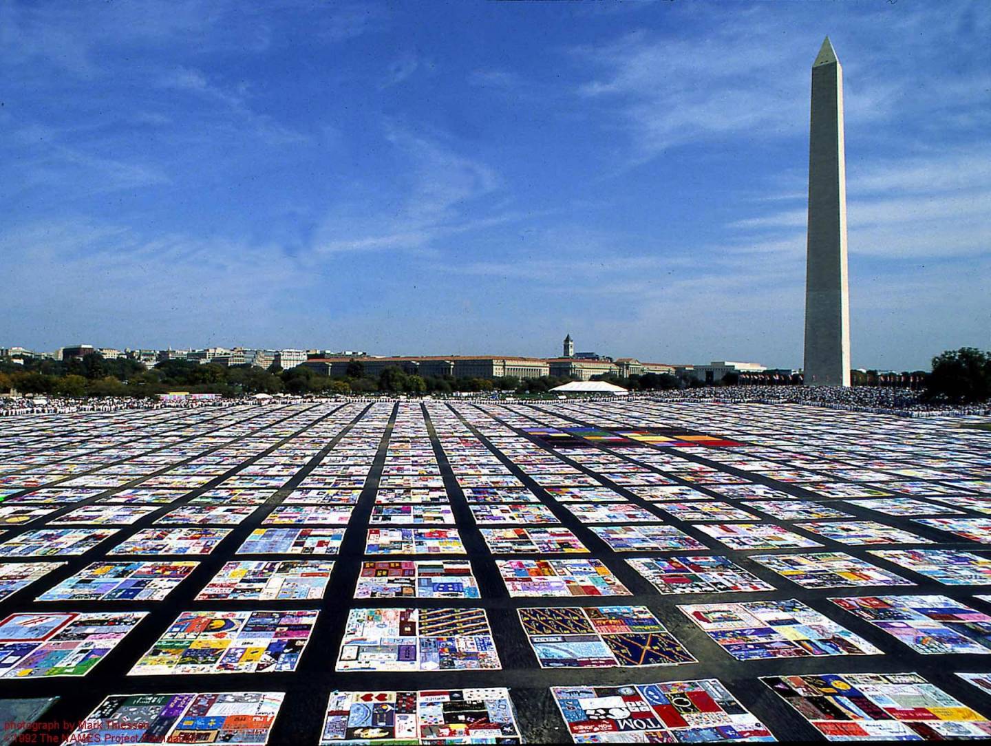 Display of AIDS quilts stretching out towards the horizon with Washington Monument in the background