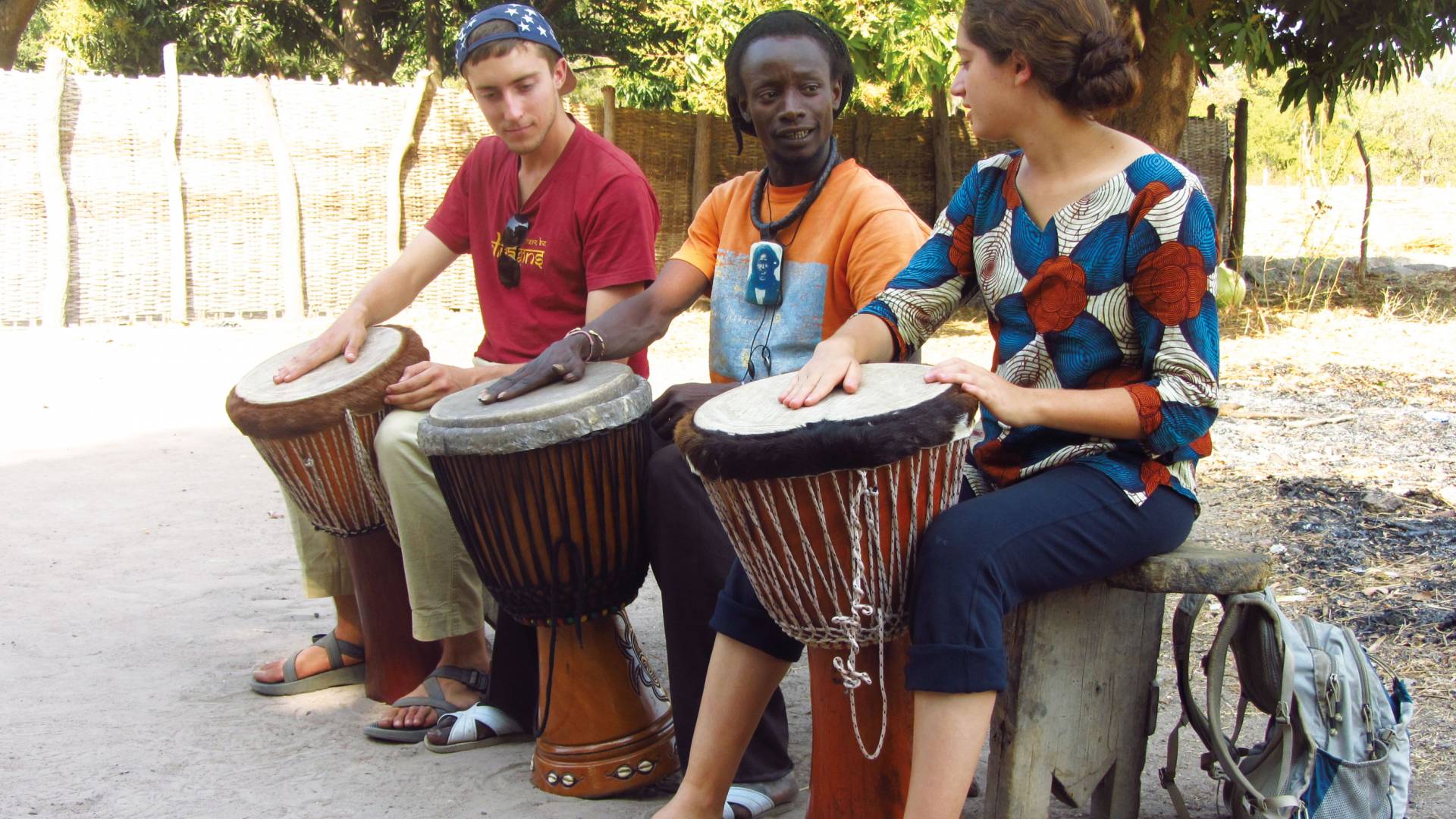 Students sit and play drums with drummer in Senegal