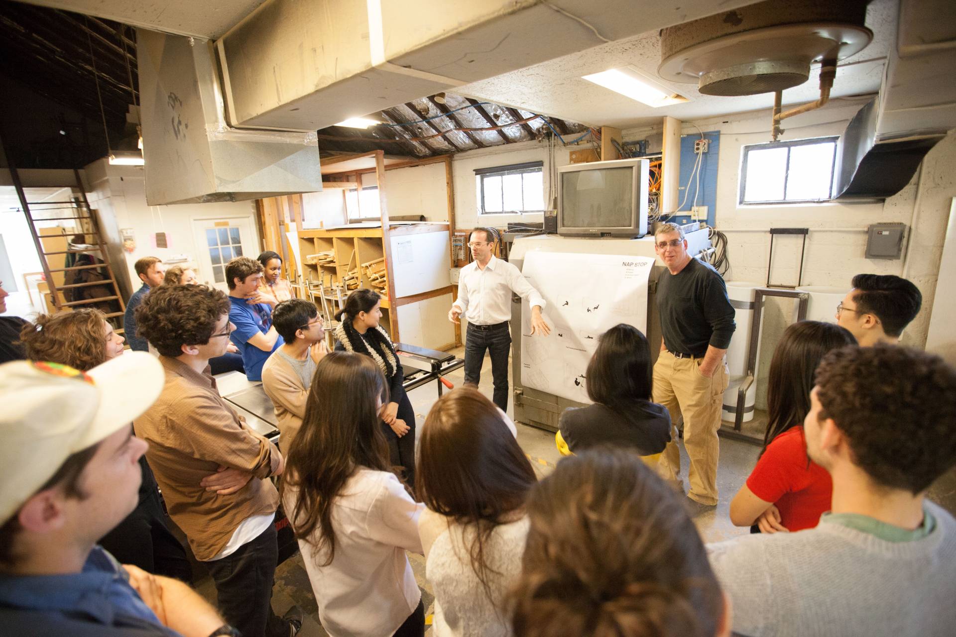A class is held in an architecture workshop, with students huddled around two professors.