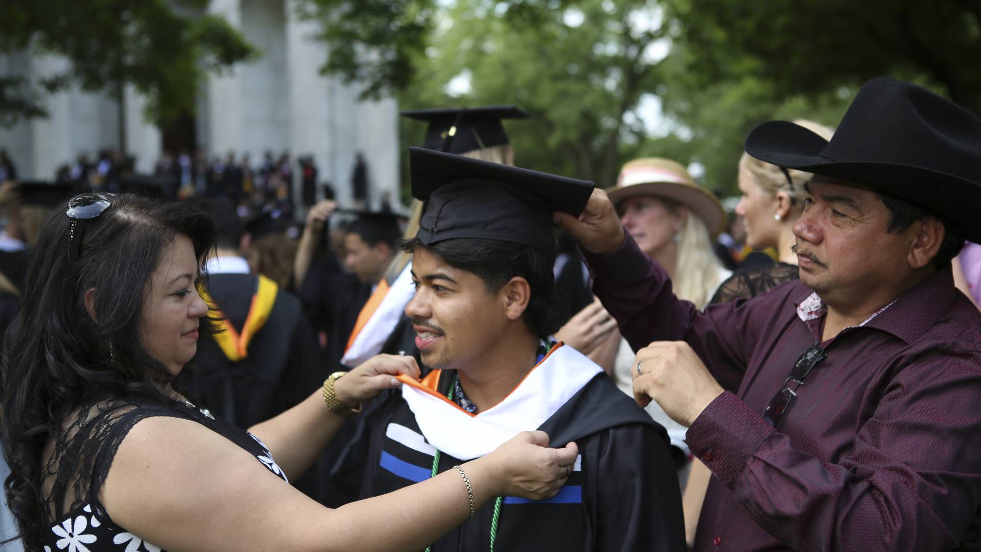 Fidelina Martinez (left) and Juan Leiva (right), natives of El Salvador who live in Trenton, New Jersey, help their son Gerson Leiva (center), the first in his family to go to college, get ready before the processional.