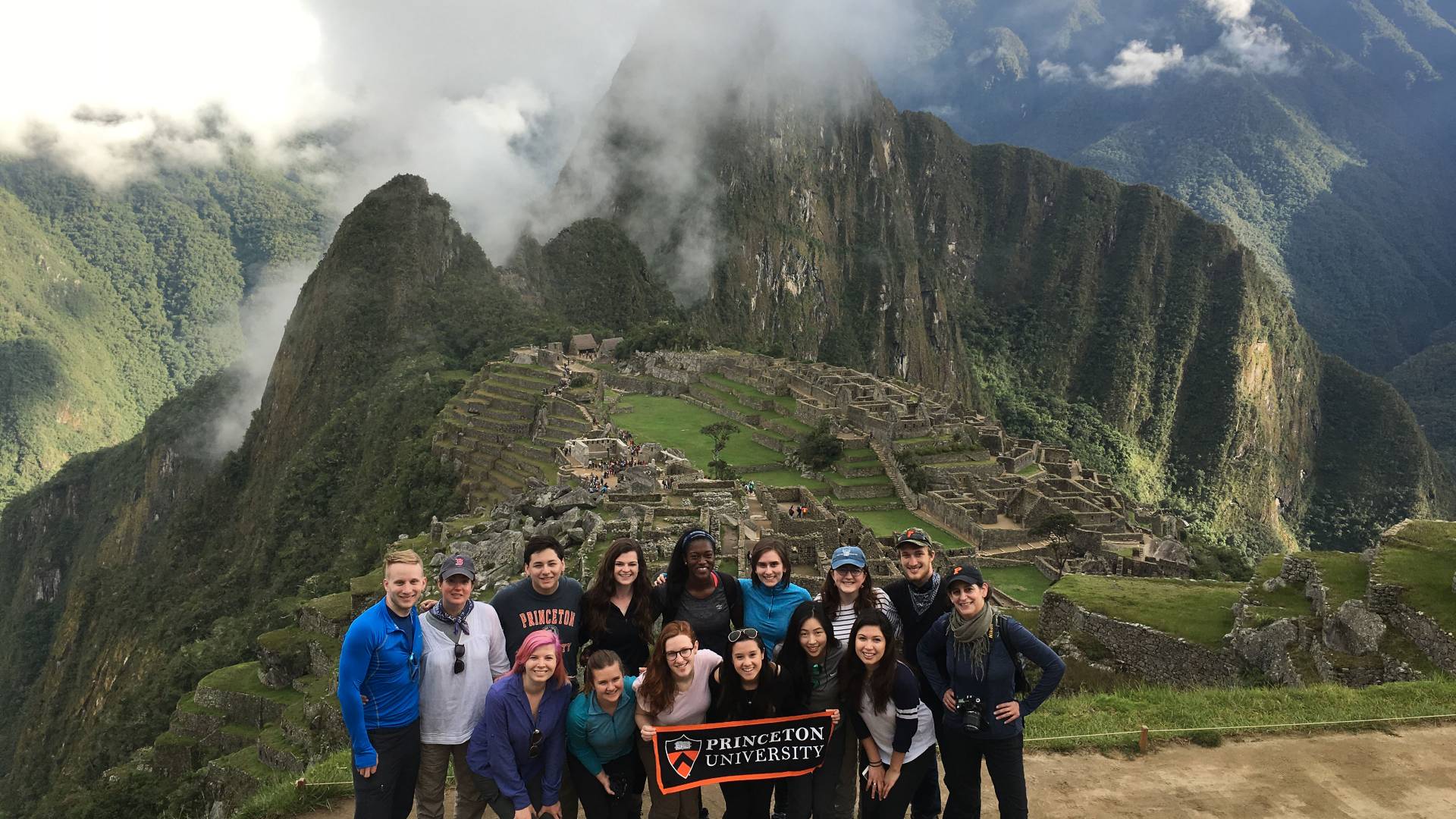 Students stand in a group holding a Princeton University banner in front of Machu Picchu