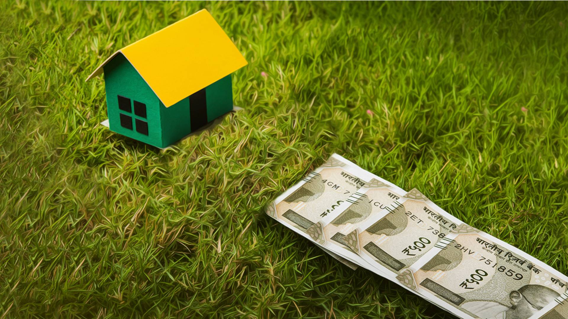 Small house on grass near a stack of rupees