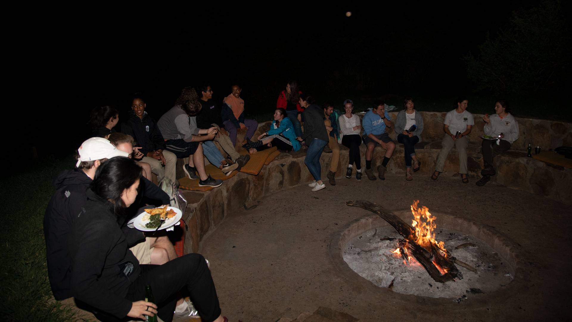 Students sitting around a campfire at night at Mpala