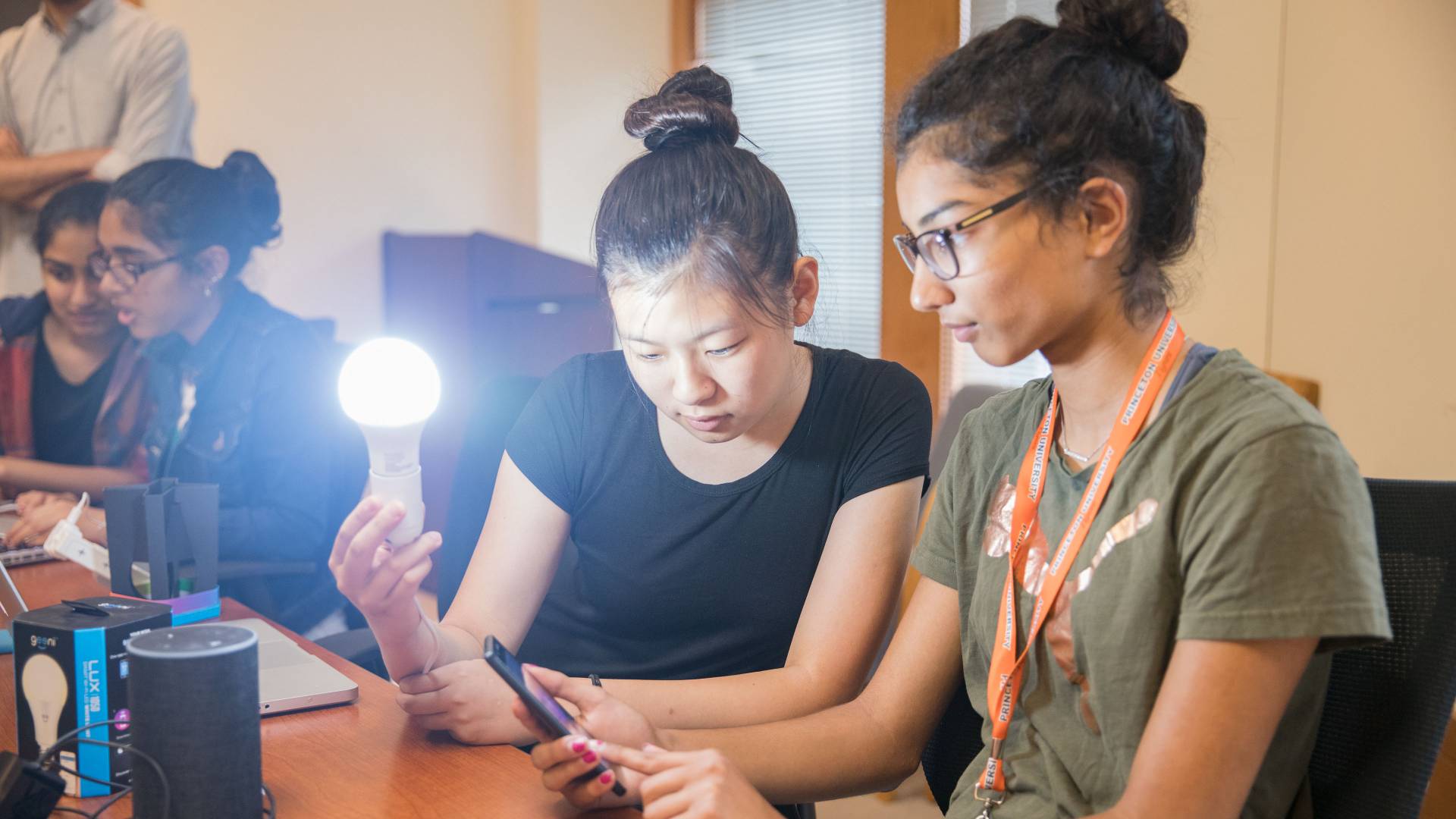 Students holding lit lightbulb while looking at cell phone