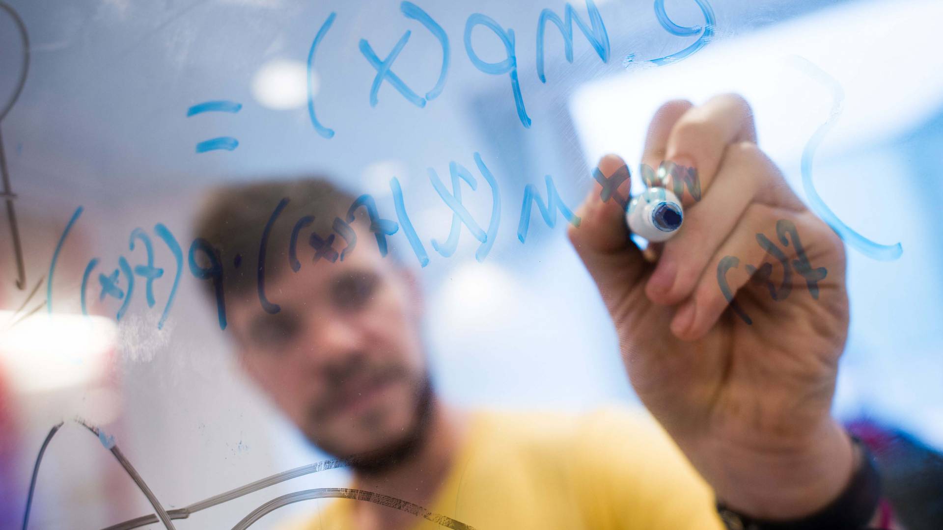A student writes math formulas on a plexiglas surface