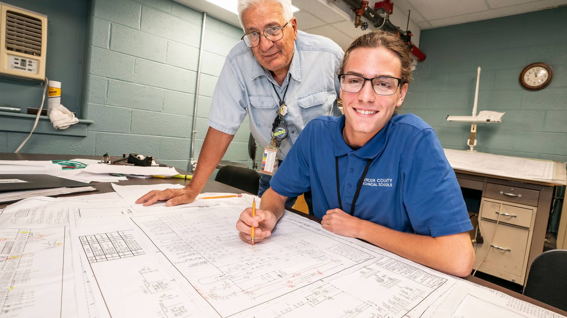 A technician and apprentice look over blueprint plans