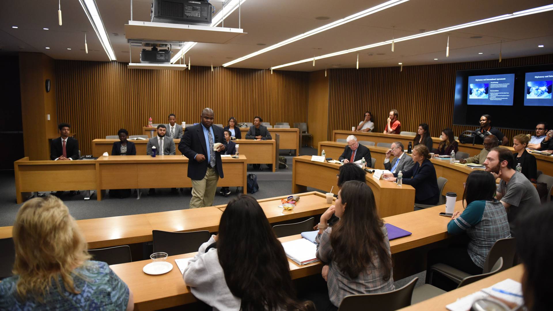 A man speaks to an auditorium-style classroom full of undergraduates