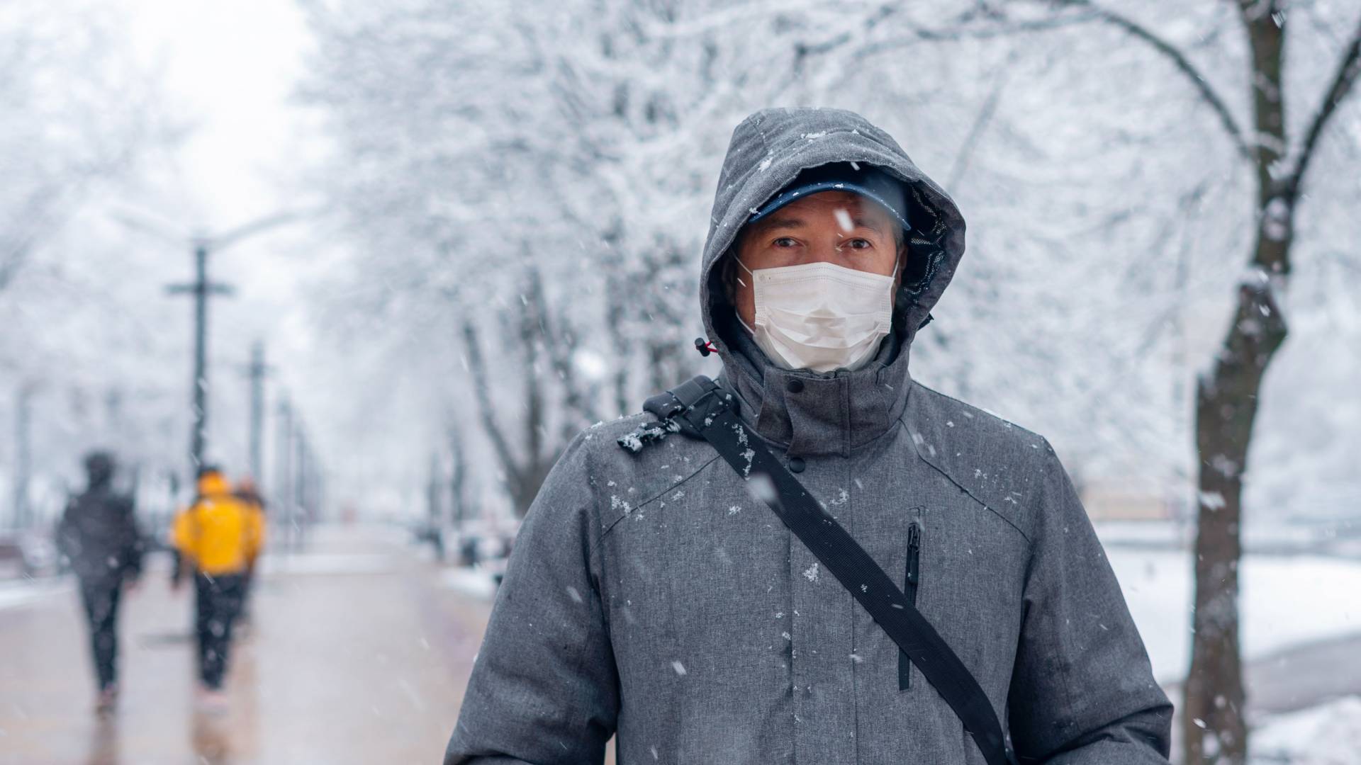 A masked person stands on a snowy walking path