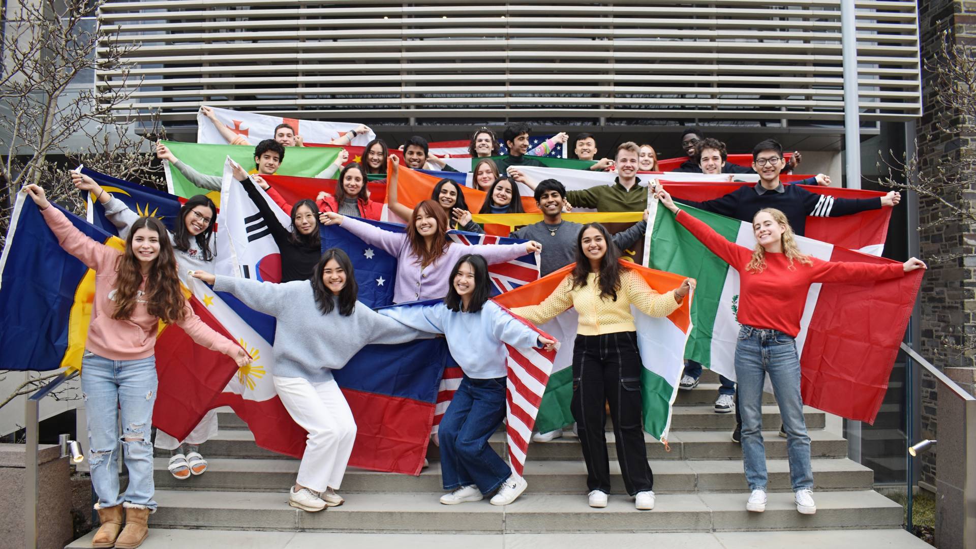 International Students holding the flags of their home nations pose on a stairway near the Davis International Center