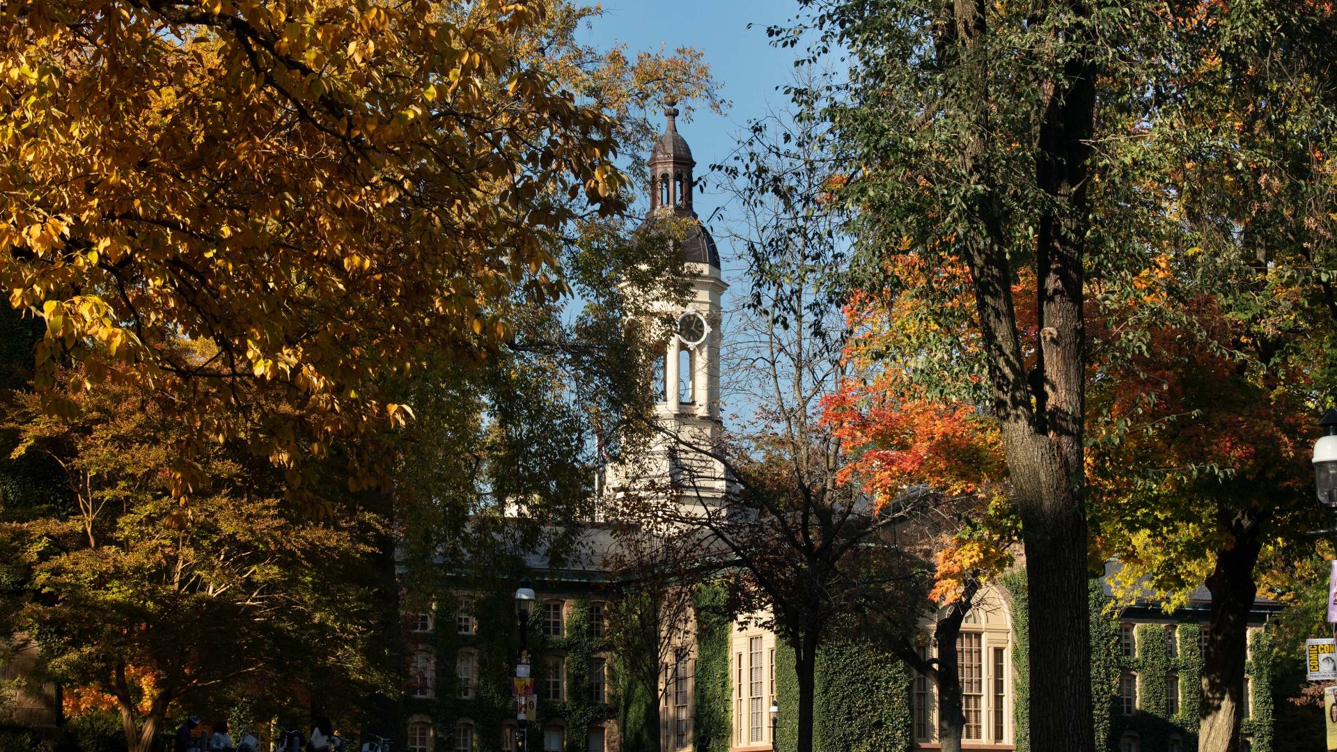 Fall-colored trees slightly obscuring a view of the back of the Nassau Hall building on Princeton's campus