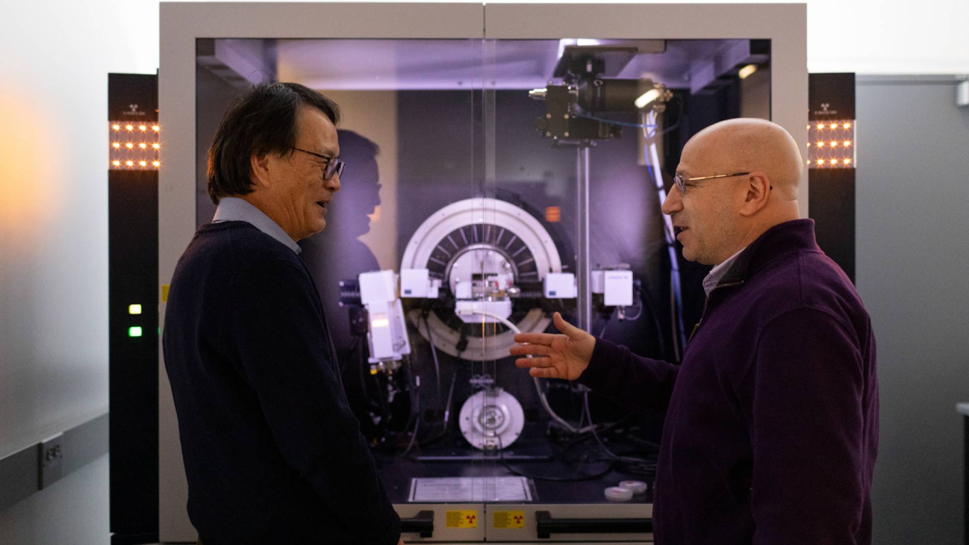 Two scientists stand in front of a large, shiny machine.