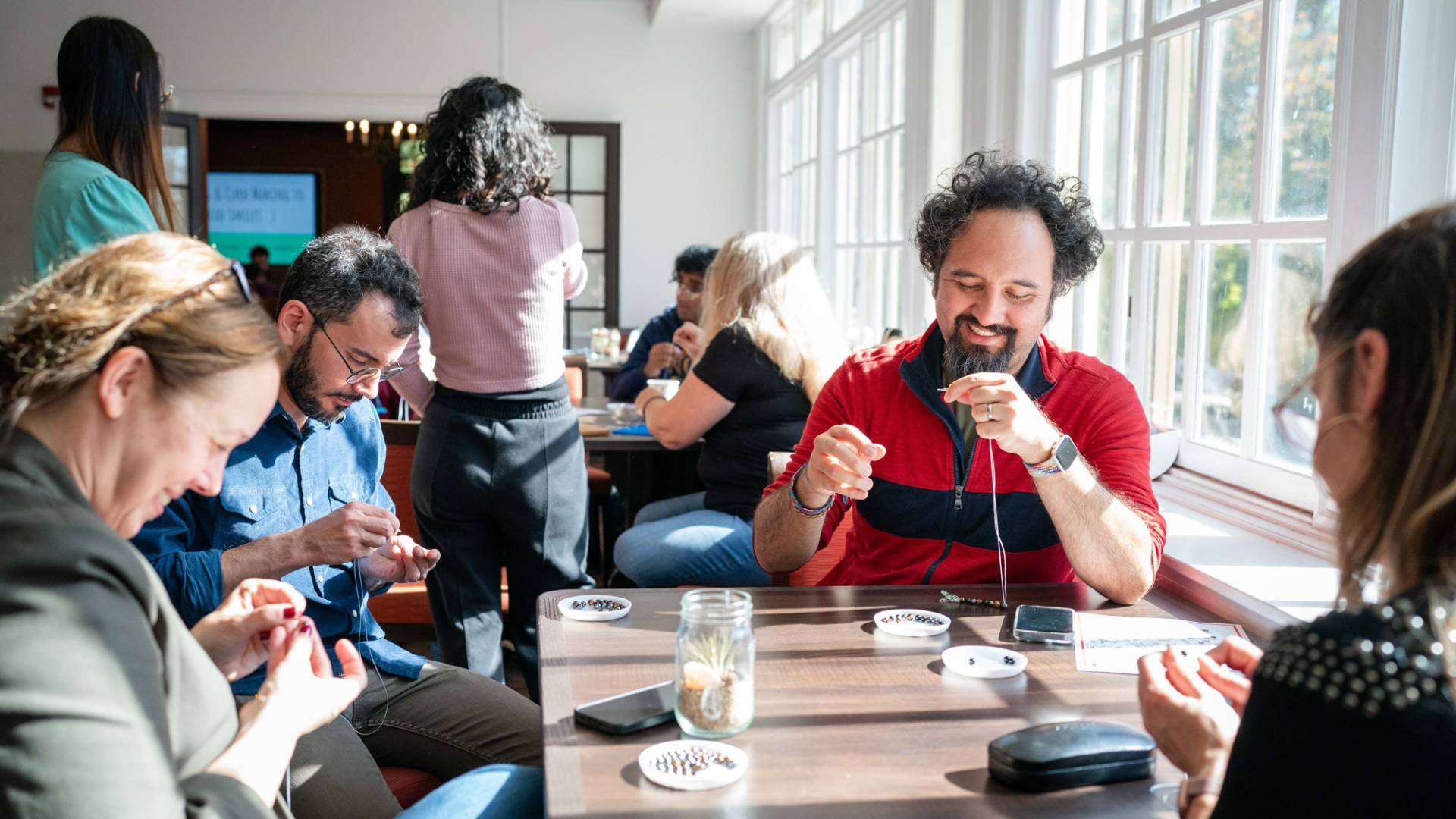 A group of people gather around a table making bracelets.