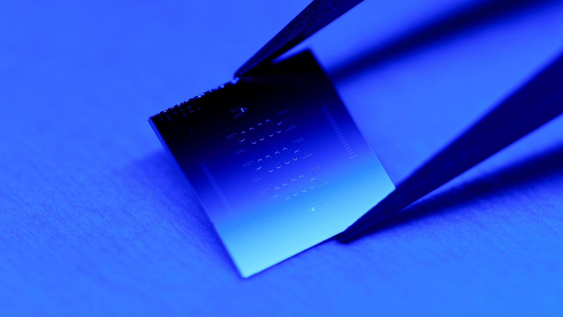 A pair of tweezers carefully places a small, wafer-thin square of metal.