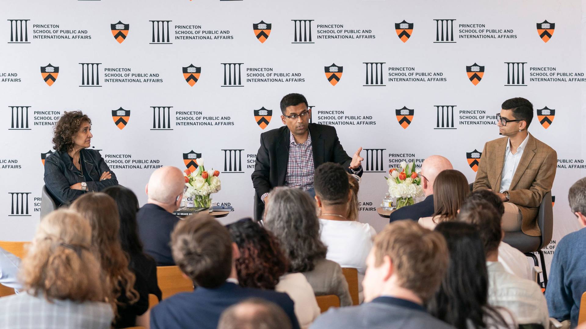 Scholars in a crowded panel discussion sit in conversation against a white backdrop accented with Princeton crests to discuss AI policy