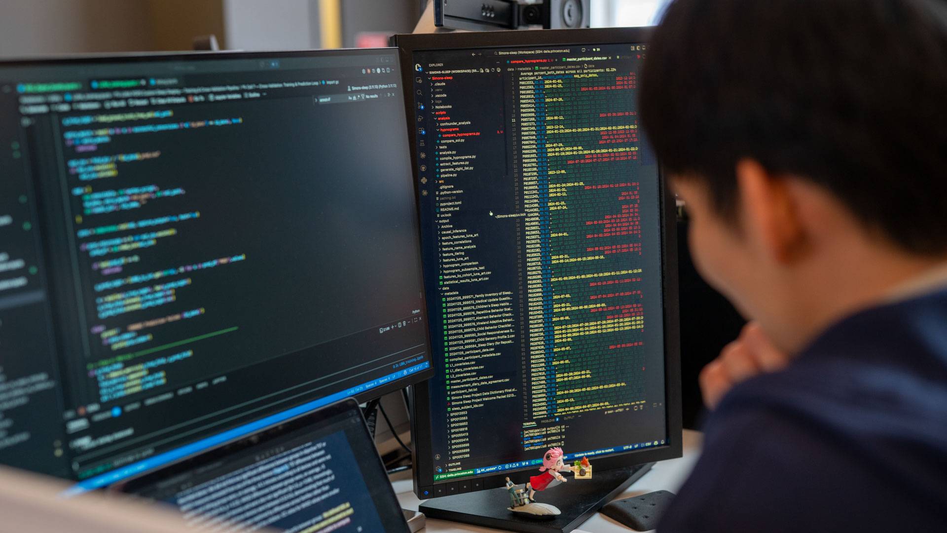 A researcher consults columns of data displayed on three computer monitors