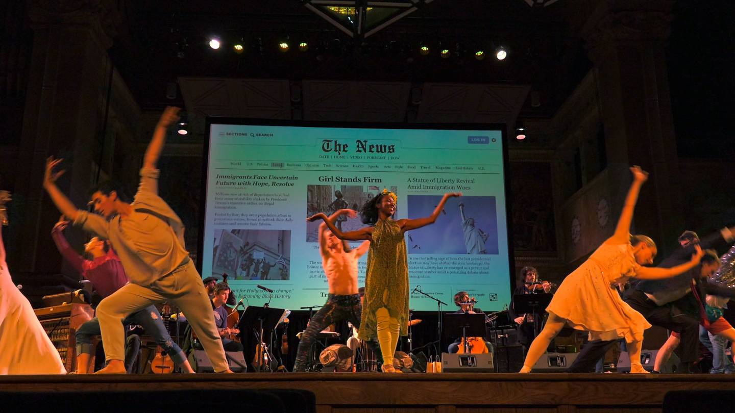 Students dancing on stage with orchestra and artwork projected on back screen