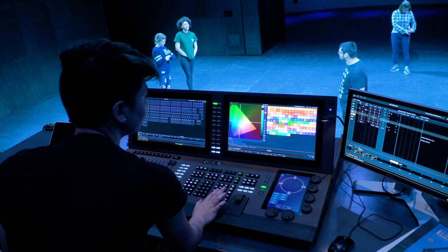 Student running lighting board with actors on stage