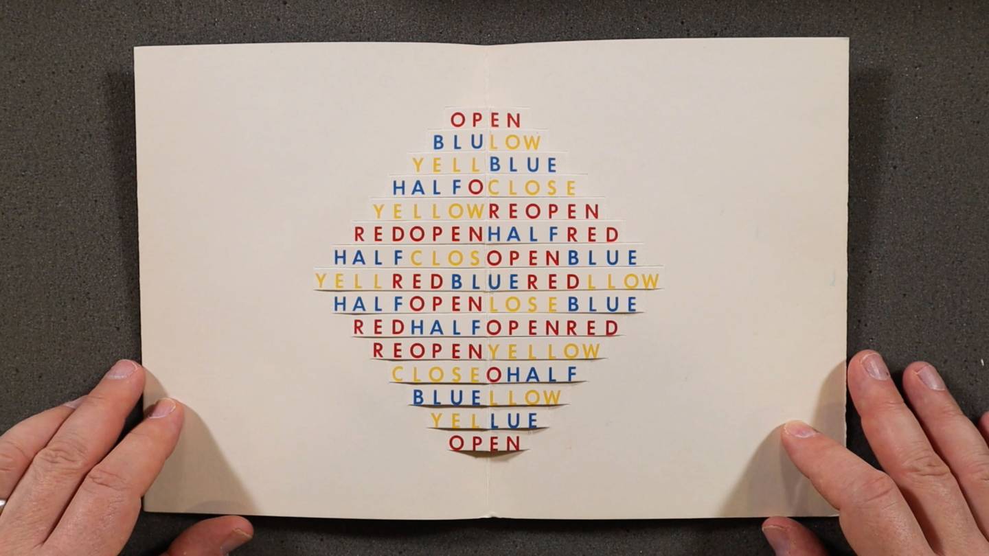 pair of hands opens a book with cuts that form a 3-dimensional diamond shape with words like "BLUE," "OPEN," "RED" and "HALF"