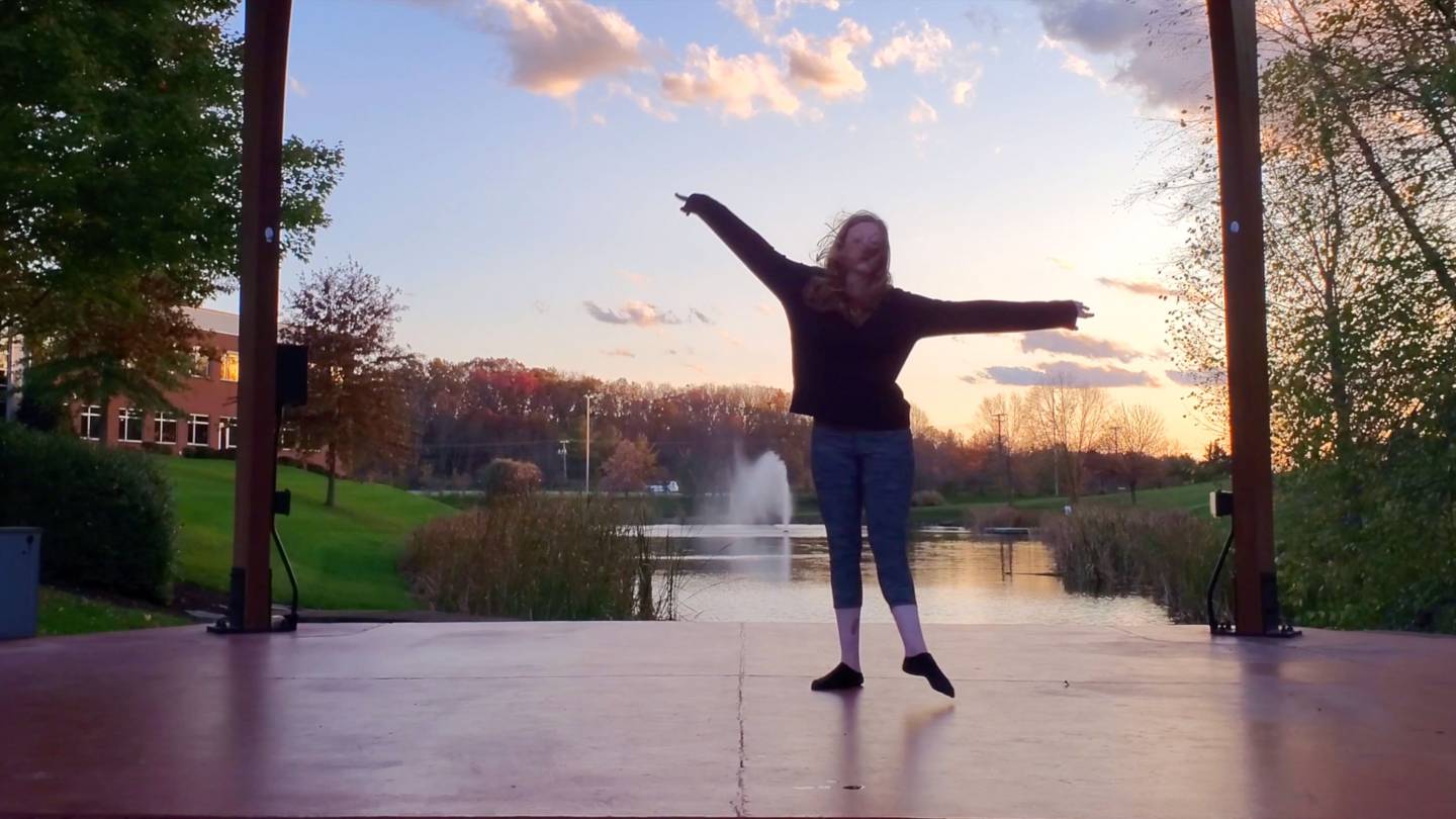 A dancer at twilight dancing in front of a fountain in a pond