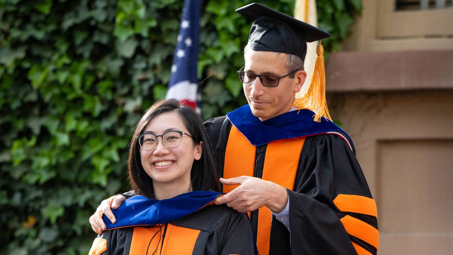 A graduate student is hooded by a professor