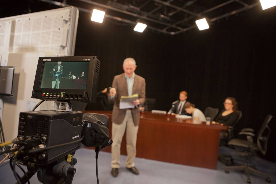 Professor stands in front of a camera recording a lecture