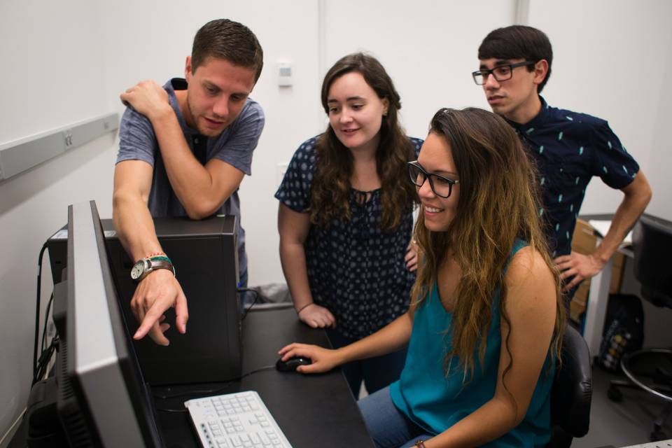 Graduate students gather around a computer while one student points at the screen