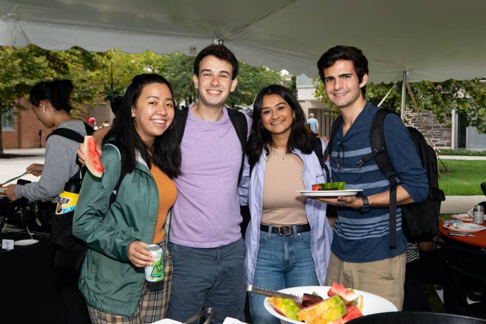 Four students pose for camera at Department of Economics barbeque in tent.