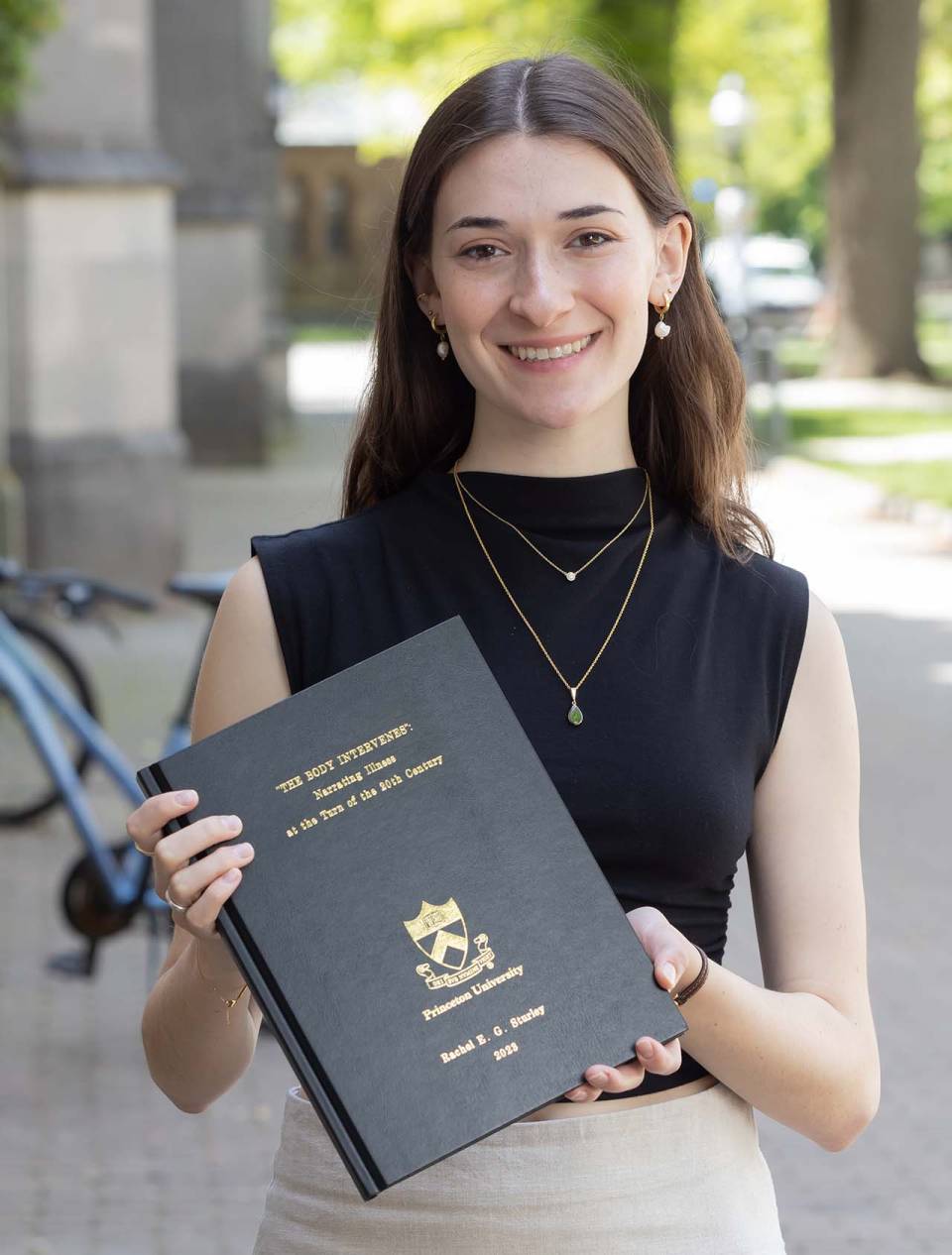 Rachel Sturley smiling while holding her thesis book.