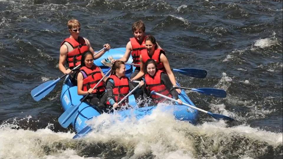 Students whitewater rafting in orange vests, blue raft