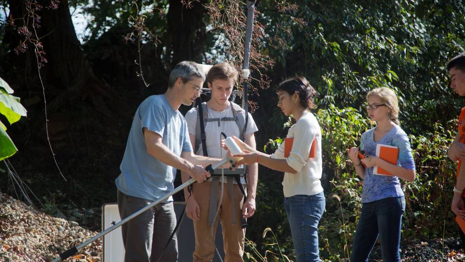 In the woods, a professor shows students how to use a scanning device.