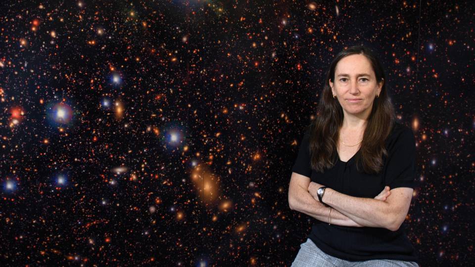 Eve Ostriker sits in front of a satellite photo of stars and planets