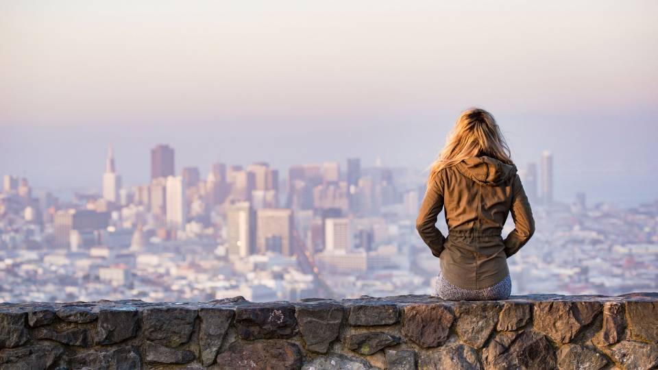 Girl sitting on a stone wall looking out over a city
