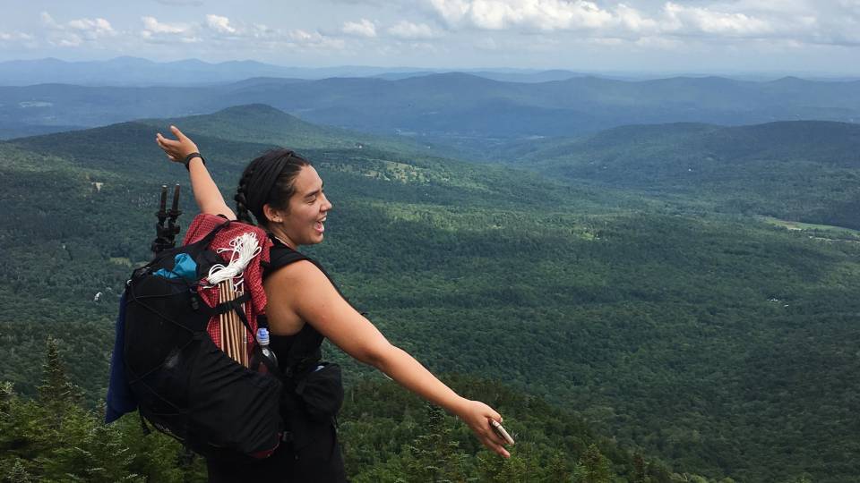 Tess Jacobson stretches out her arms in joy facing a mountainscape