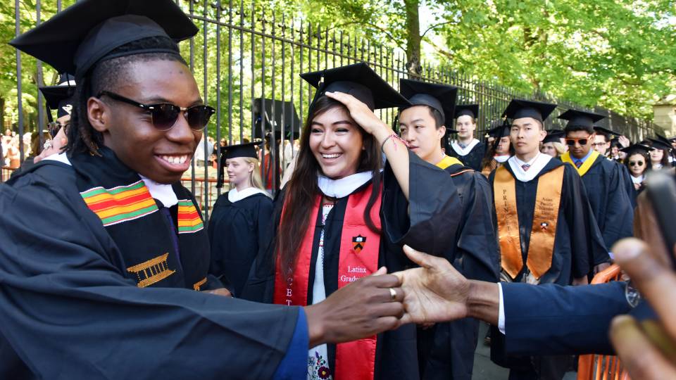 Student shaking hands with onlooker while processing toward campus for Commencement