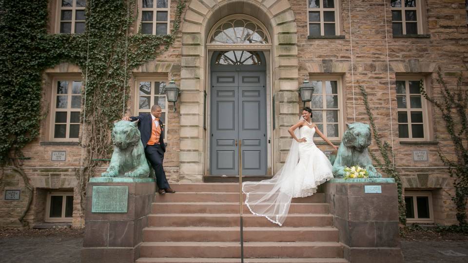 A bride and groom pose in between the two tigers in front of Nassau Hall