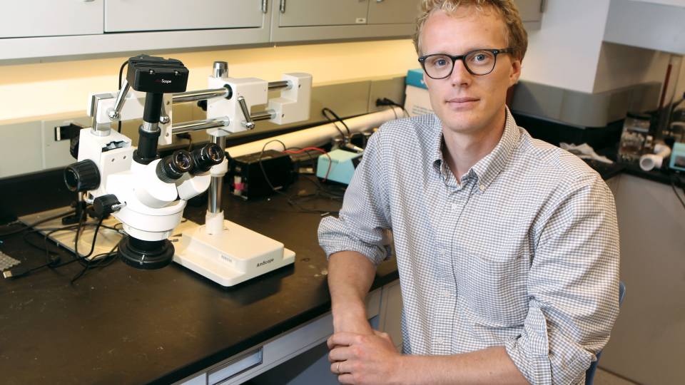 Marcus Hultmark sits next to a microscope in a laboratory