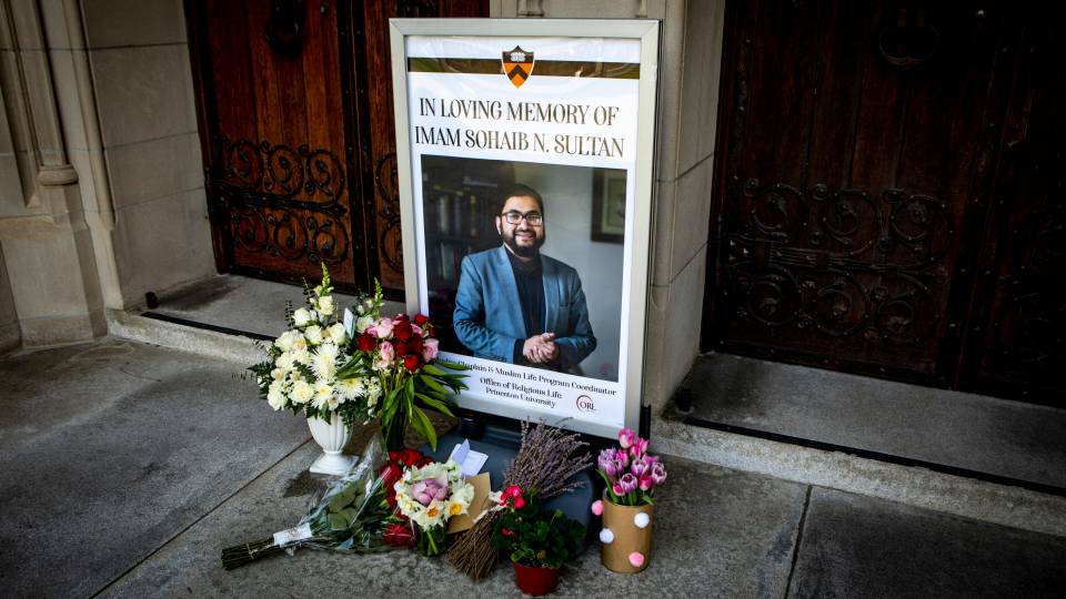 A poster in front of chapel doors, reading, "In Loving Memory of Imam Sohaib N. Sultan" and flowers