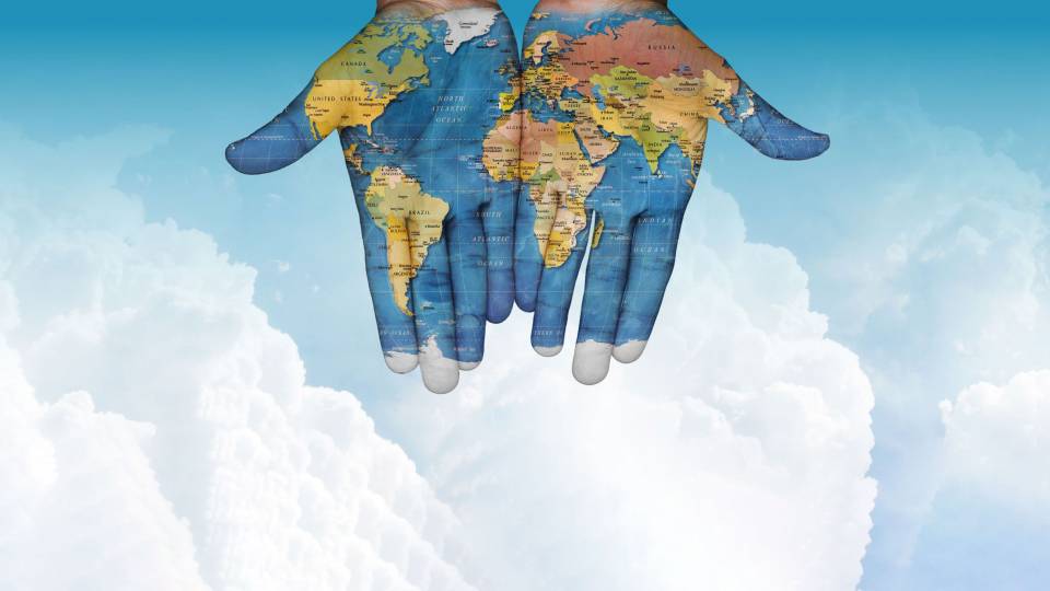 open hands painted with a map of the world with puffy clouds and blue sky in the background