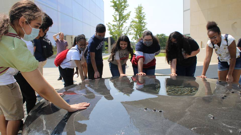 Students place hands on the Maya Lin fountain sculpture installation